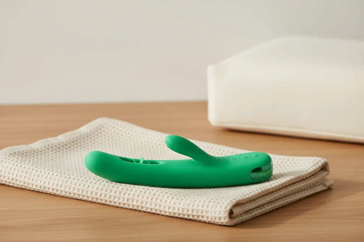 VINDANI Empower Green G-spot wellness device resting on a folded ivory towel beside a wedge cushion in a calm spa setting